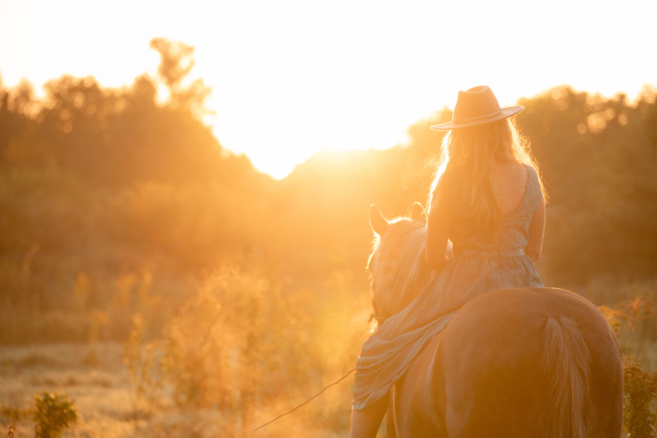 Frau mit Sonnenhut auf einem Pferd vor einem Sonnenaufgang