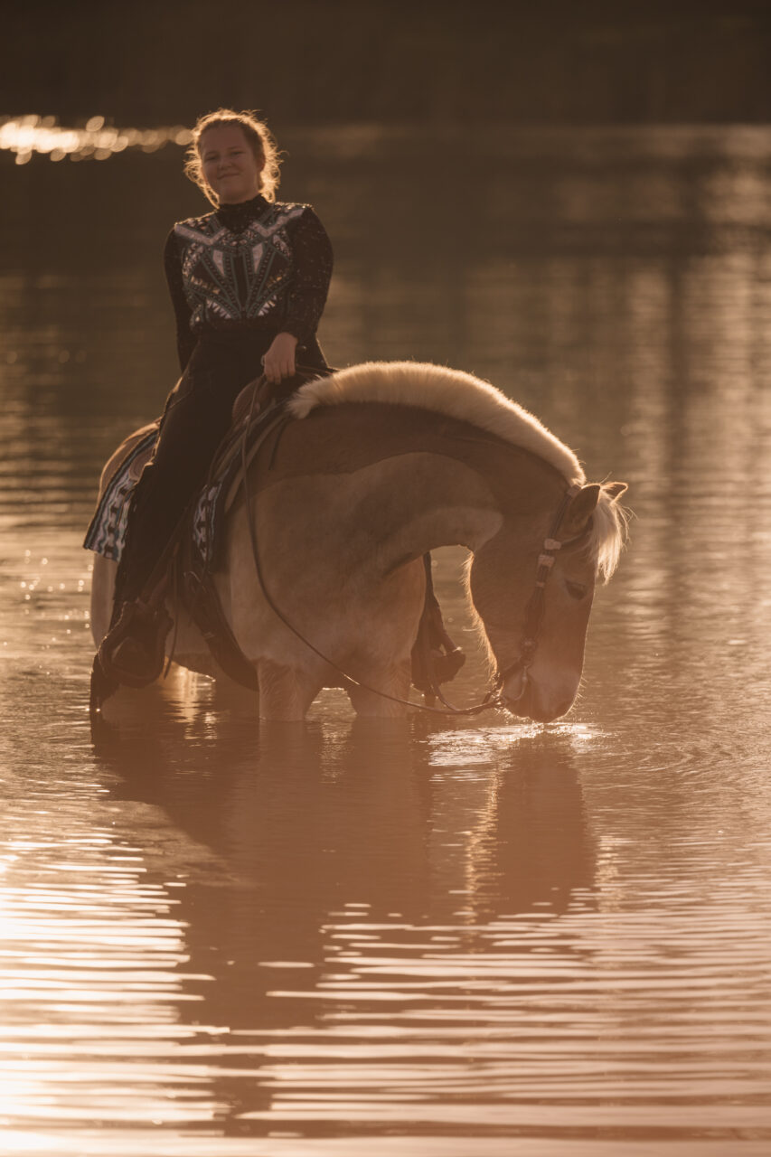 Frau auf Pferd, dass bis zum Bauch im Wasser steht.